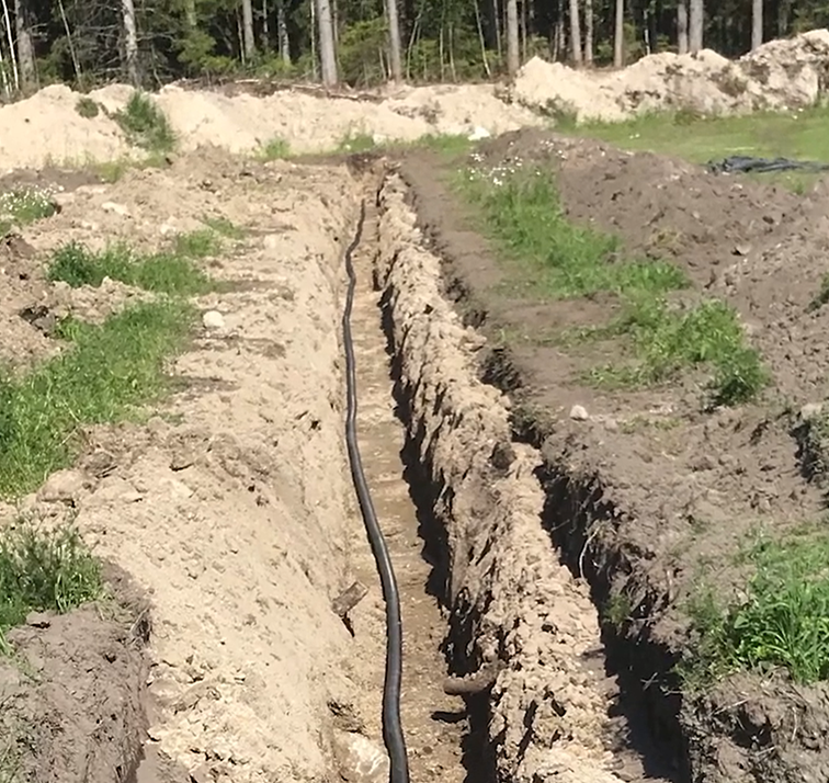 jordhauger og et rør er lagt ned i en oppspadd grøft, gresstuster og skog i bakgrunn - Klikk for stort bilde