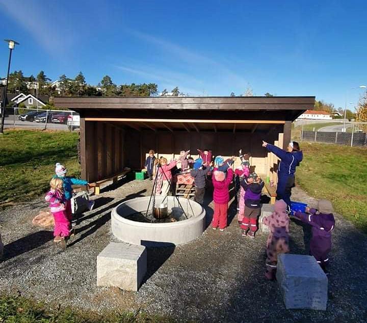 Barnehagebarn samlet rundt bålpanne ved en gapahuk bygd i tre. - Klikk for stort bilde