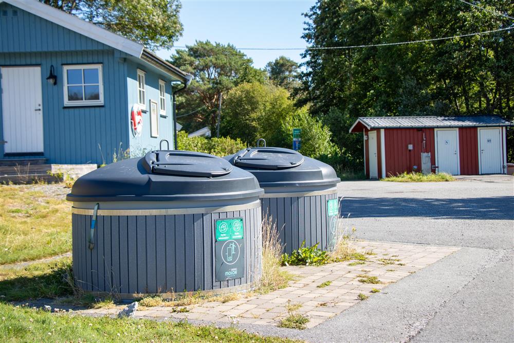To runde søppeldunker som står ved en vei, blått og rødt bygg i bakgrunn. - Klikk for stort bilde