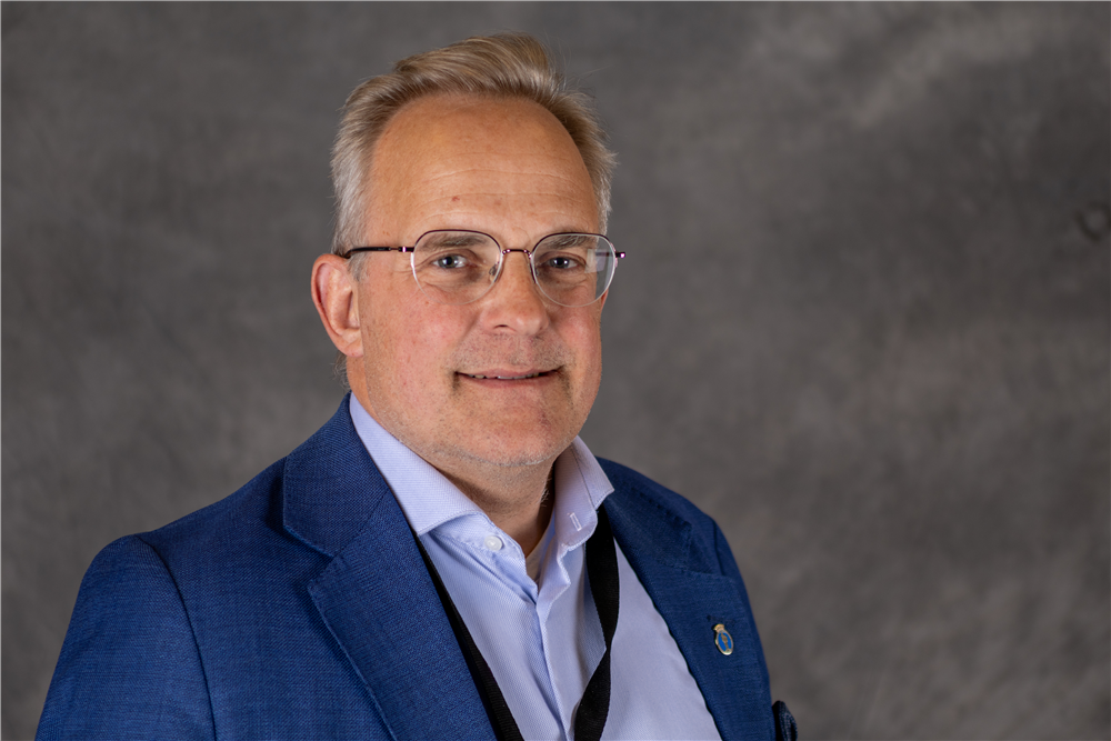 Mann med lyst kort hår og briller har på seg blå blazer og lyseblå skjorte - Klikk for stort bilde