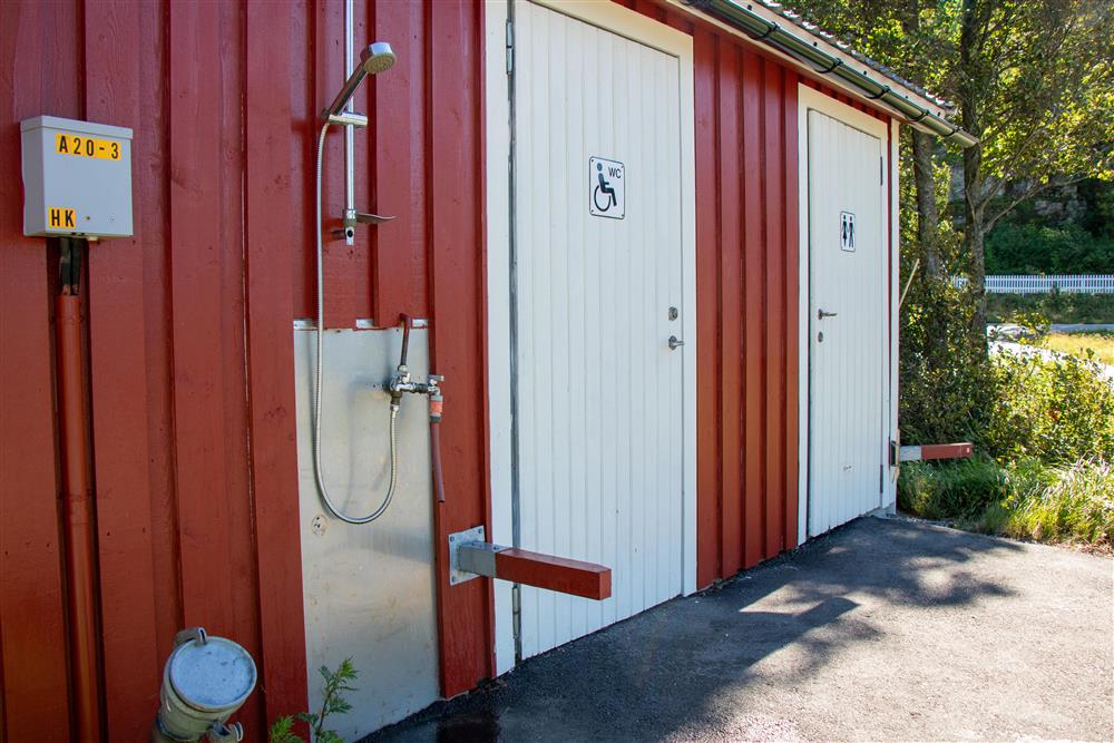 Lite rødt trebygg med to hvite dører og en utedusj montert på veggen. - Klikk for stort bilde
