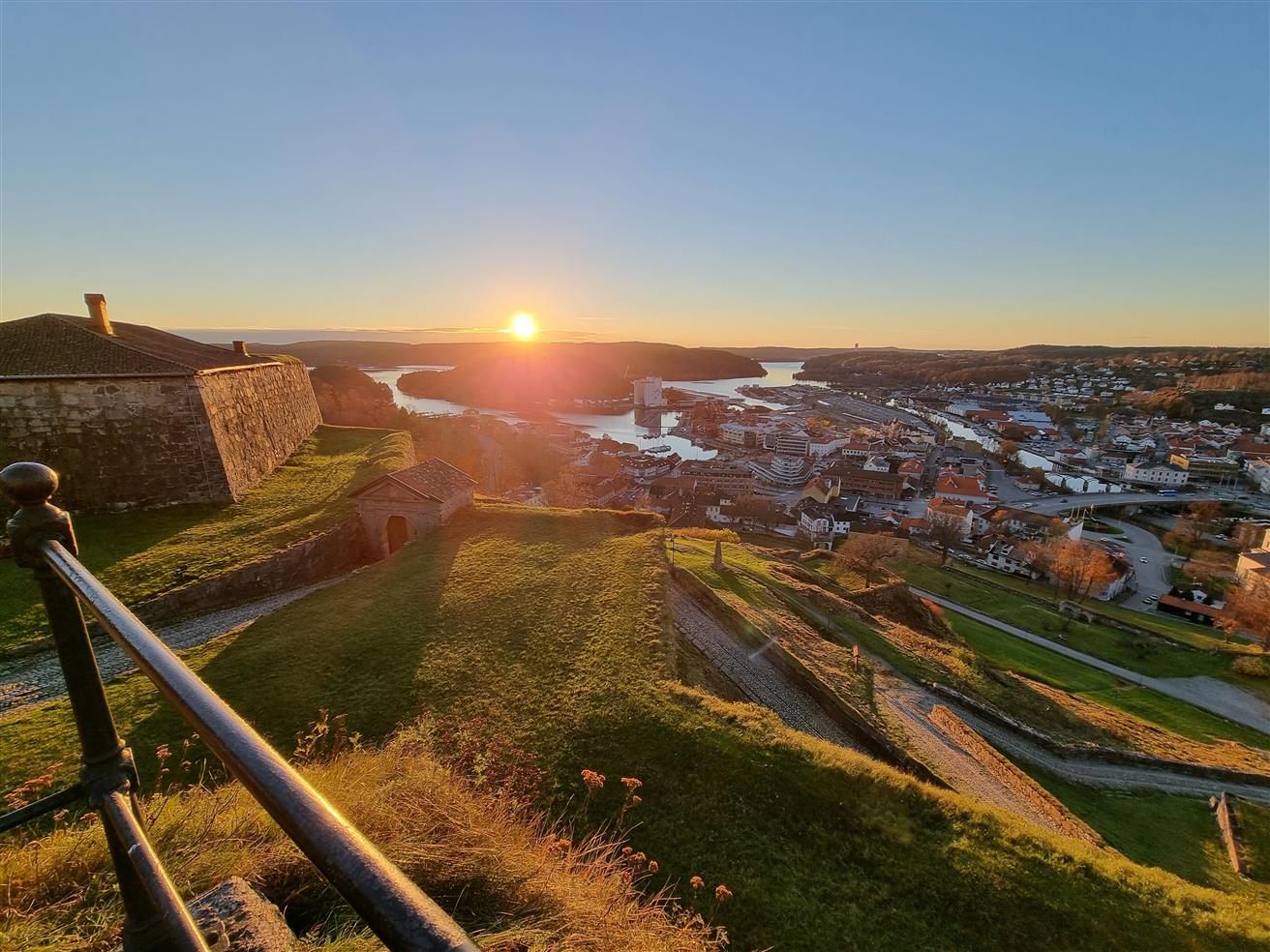 Bysentrum og havn med blå himmel og solnedgang sett fra en høyde med grønt gress