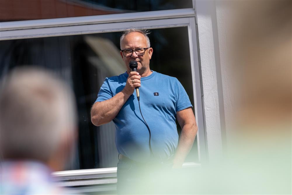 Mann i blå trøye snakker i mikrofon - Klikk for stort bilde