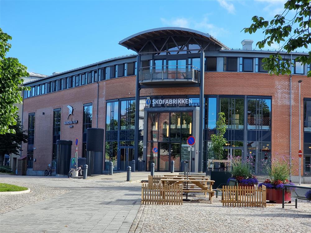 en bygning med stort inngangsparti i glass, mur og med steinsatt område foran - Klikk for stort bilde