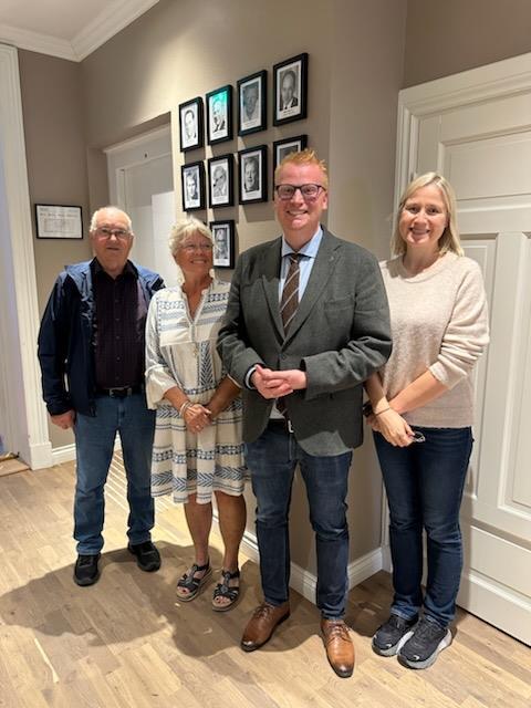 To menn og to damer oppstilt foran vegg med fotografier i ramme.  - Klikk for stort bilde