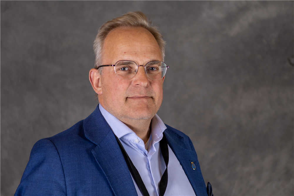 Mann med lyst kort hår og briller har på seg blå blazer og lyseblå skjorte - Klikk for stort bilde